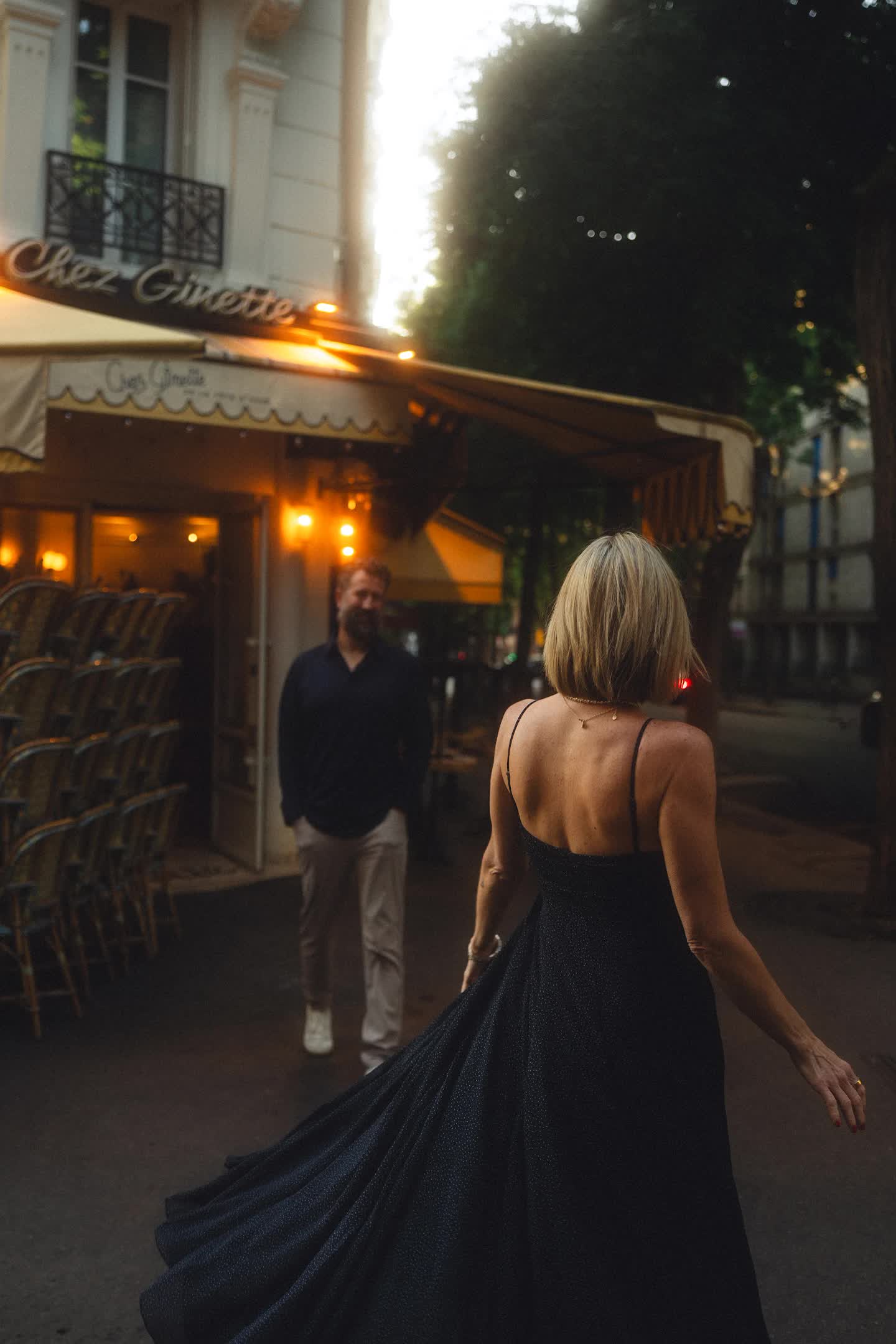 Couple walking past a Paris café at dusk